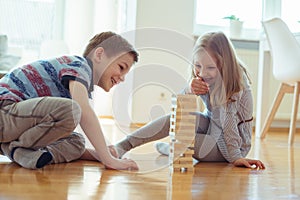Two happy siblings playing a game with wooden blocks at home