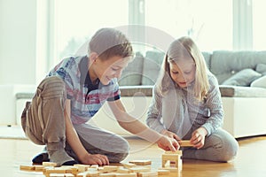 Two happy siblings playing a game with wooden blocks at home