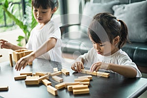 Two happy siblings playing a game with wooden blocks at home joyfully