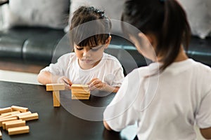 Two happy siblings playing a game with wooden blocks at home joyfully