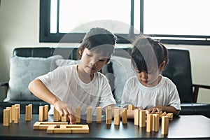 Two happy siblings playing a game with wooden blocks at home joyfully