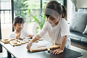 Two happy siblings playing a game with wooden blocks at home joyfully