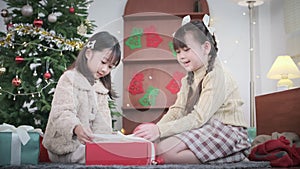 Two happy siblings sitting on floor in beautiful festive living room unpacking Christmas gift boxes