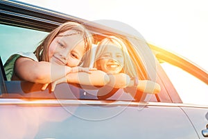 Two happy sisters looking out open car window during auto trip. Cute girls are smiling, laughing during road jorney. Family values photo