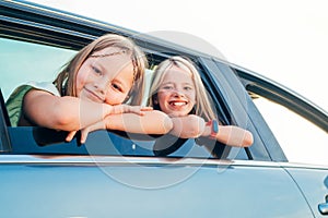 Two happy sisters looking out open car window during auto trip. Cute girls are smiling, laughing during road jorney. Family values photo