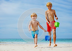 Two happy smiling boys run with water buckets from sea waves