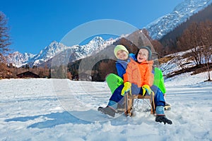 Two happy smiling boys on the sledge going downhill at mountains