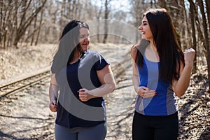 Two happy smiling fit and overweight women friends jogging in th