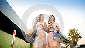 Two happy smiling girls with paper bags walking on street after doing shopping in mall