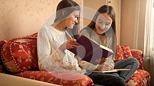 Two happy smiling girls smiling and laughing while doing homework and writing in copybooks or diaries