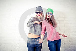 Two Happy Smiling Hipster Girls at White Wall