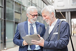 Two happy smiling senior gray haired businessmen working on a tablet