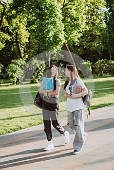 Two happy smiling student girls are walking and talking to each other on campus on a warm sunny day. Soft selective focus