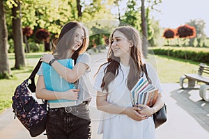 Two happy smiling student girls are walking and talking to each other on campus on a warm sunny day. Soft selective focus