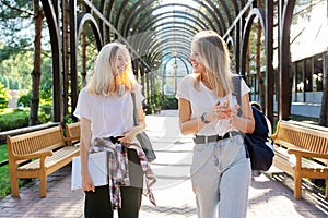 Two happy smiling talking girls teenagers students walking together