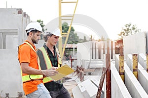 Two happy smiling worker engineers with safety vest and helmet inspecting working area at construction site. Architect working