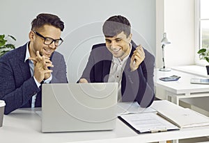 Two happy successful business people using laptop computer while working in the office