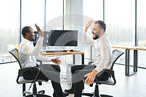 Two happy successful excited diverse traders investors giving high five celebrating successful stock exchange trading