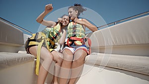 Two happy teen girls wearing safety belts dancing on a yacht