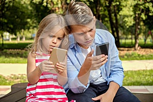 Two happy teenage friends using on mobile phone while relaxing in the park. Problems of modern youth, social networks