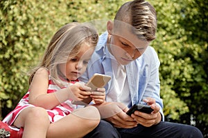 Two happy teenage friends using on mobile phone while relaxing in the park. Problems of modern youth, social networks