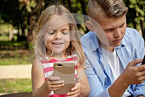 Two happy teenage friends using on mobile phone while relaxing in the park. Problems of modern youth, social networks