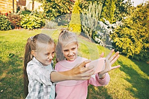 Two happy teenage girls laugh and take a selfie on a cell phone outdoors.