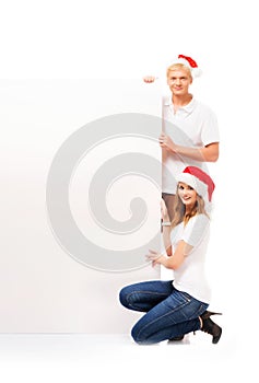 Two happy teenagers in Christmas hats holding a banner