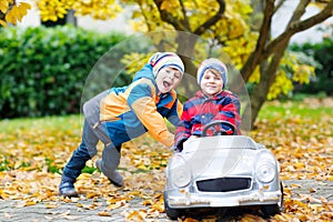 Two happy twins kids boys having fun and playing with big old toy car in autumn garden