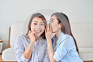 Two happy women with eavesdrops whispers a secret mystery in the studio on living room