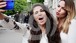 Two happy women friends make selfie on the phone on the street