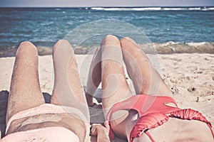 Two happy women friends sunbathing on the tropical beach of Bali island, Nusa Dua, Indonesia.