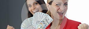 Two happy women are holding fan of one hundred dollar bills