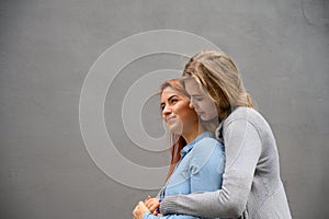 Two happy women hugging against the background of a gray wall. Gentle hugs of a female lesbian couple. LGBT Same-sex