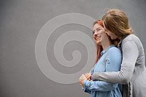 Two happy women hugging against the background of a gray wall. Gentle hugs of a female lesbian couple. LGBT Same-sex