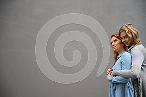 Two happy women hugging against the background of a gray wall. Gentle hugs of a female lesbian couple. LGBT Same-sex