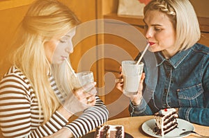 Two happy women sitting in a cafe and taking selfies on the phone, drink a cocktail