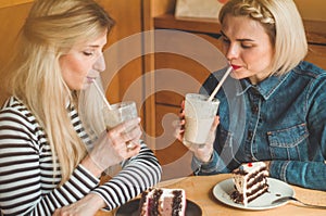 Two happy women sitting in a cafe and taking selfies on the phone, drink a cocktail