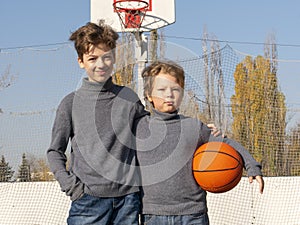 Two happy young boys on basketball field outdoors on a sports ball