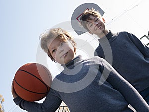 Two happy young boys playing basketball outdoors on a sports field