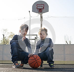 Two happy young boys playing basketball outdoors on a sports field