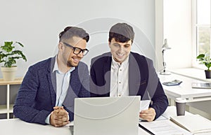 Two happy young business men working in the office and using a laptop computer together