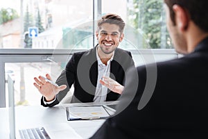 Two happy young businessmen sitting and working on business meeting