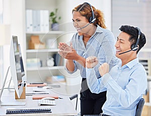 Two happy young diverse call centre telemarketing agents clapping and cheering with joy while working together in an