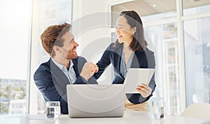 Two happy young diverse colleagues working together on a digital tablet in an office. Confident asian businesswoman and