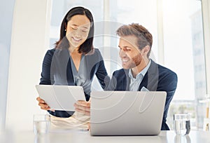 Two happy young diverse colleagues working together on a digital tablet in an office. Confident asian businesswoman and