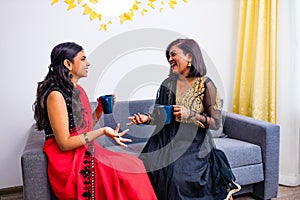 Two happy young female friends in with coffee cups in the living room at home