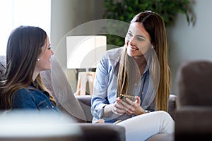 Two happy young female friends conversing in living room at home.