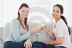 Two happy young female friends toasting wine glasses at home