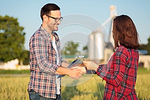 Two happy young female and male farmers or agronomists shaking hands in a wheat field photo